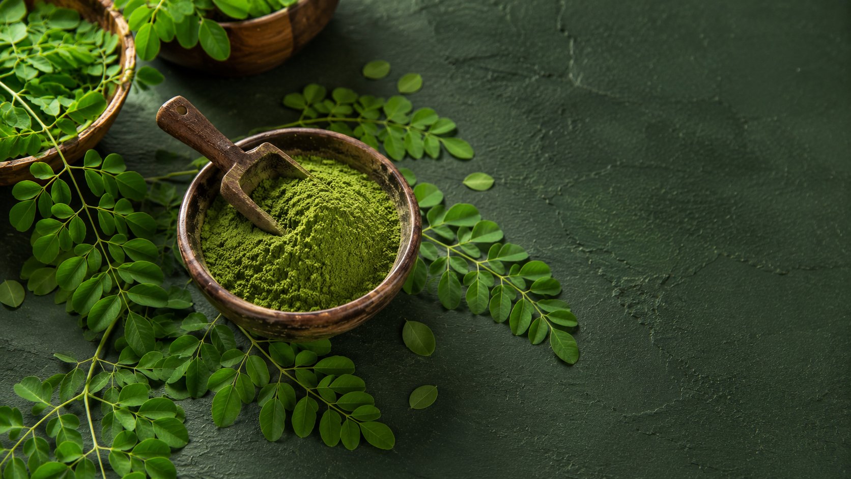 Moringa leaf powder, dried mango and dried banana chips arranged with fresh moringa leaves
